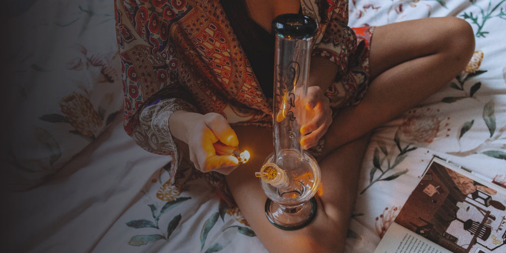 Woman sitting on bed lighting a glass bong